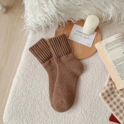 Brown socks on a textured surface with a candle, card, and book in the background.