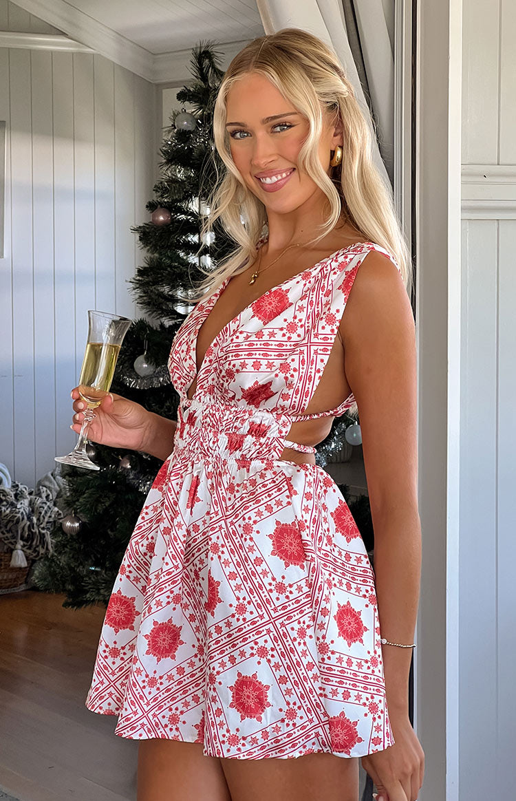 Blonde model wearing red and white print mini dress holding wine glass in front of christmas tree