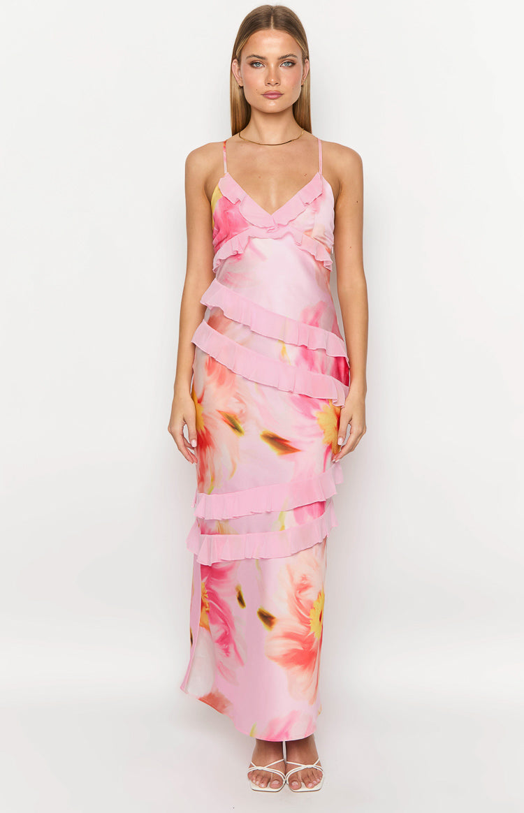 Girl facing away wearing a pink floral maxi dress and white heels holding a drink.