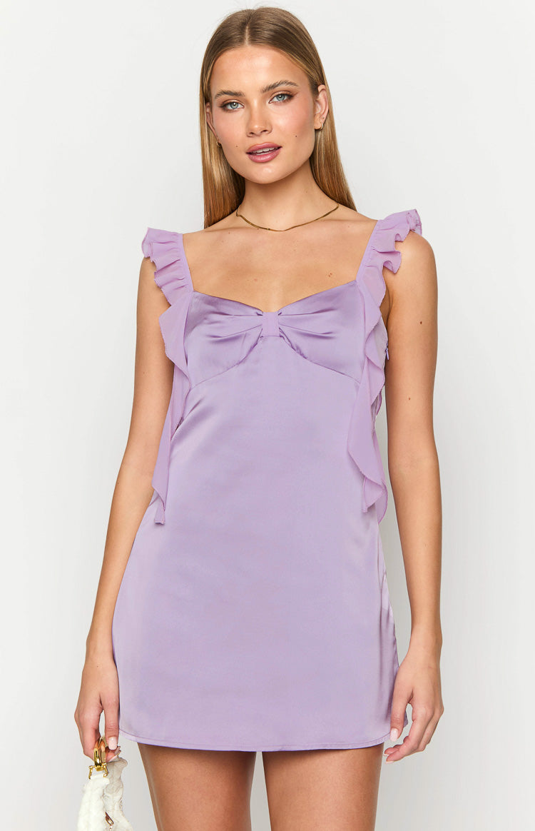 Girl facing away wearing purple mini dress in front of white table and garden.