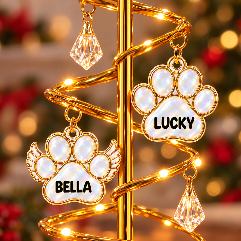Close view of LUCKY paw and BELLA winged paw name charms beside warm tree lights.