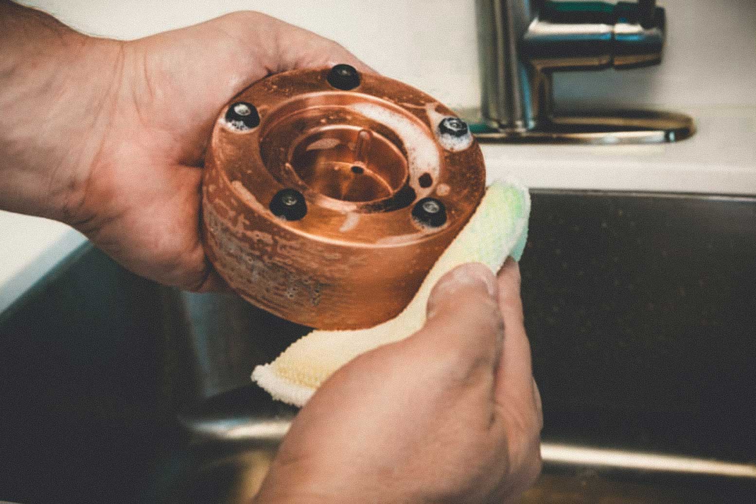 Man cleaning and polishing Meltdown Mini Mogul copper ice ball press in sink