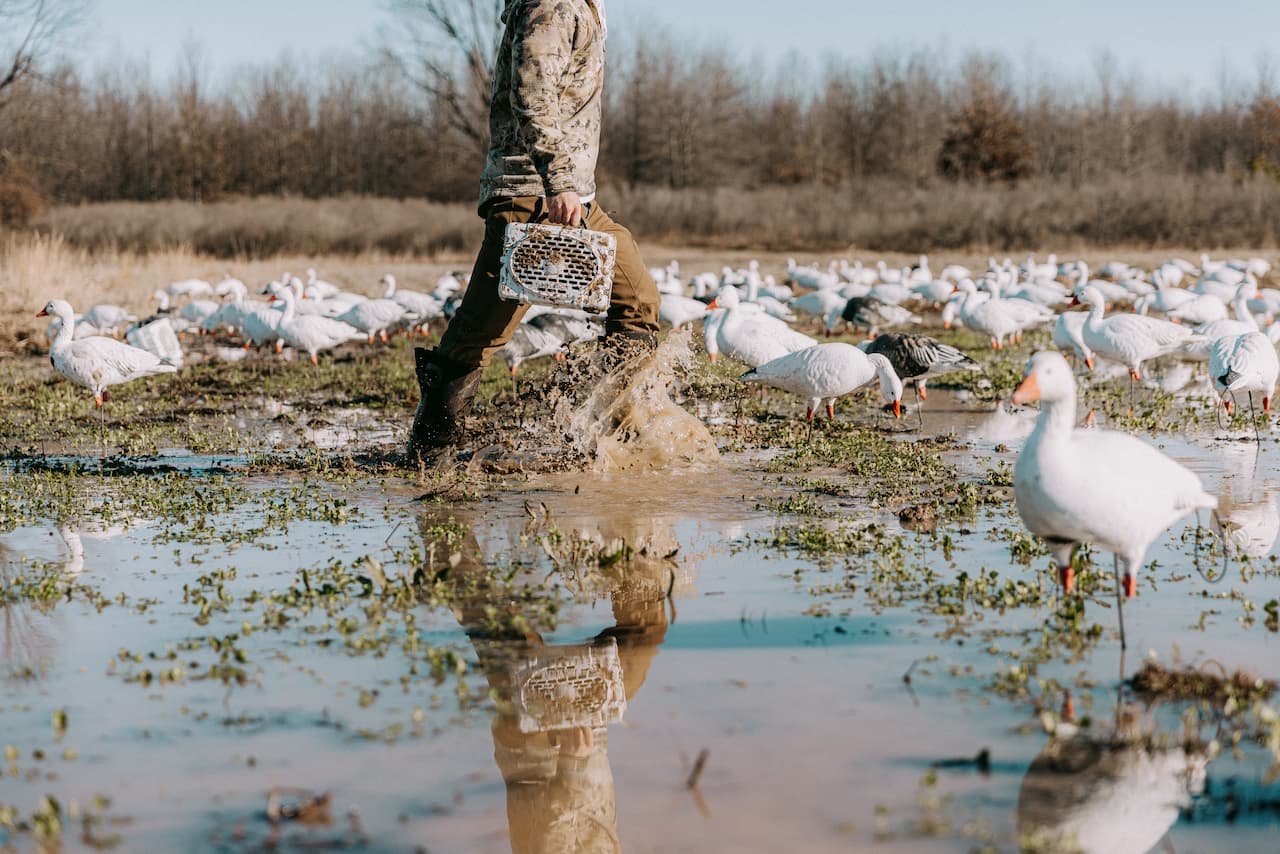 Man walking in mud with Turtlebox in hand with gooses around him.