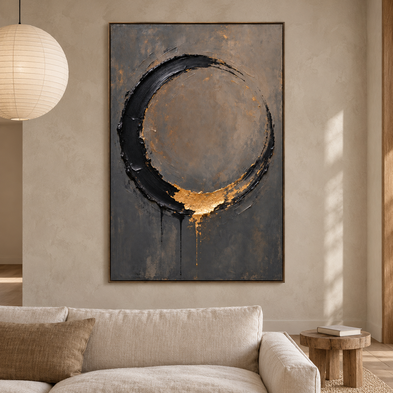 Open black brushstroke circle with a gold-colored accent at its base on warm gray, displayed in a room setting