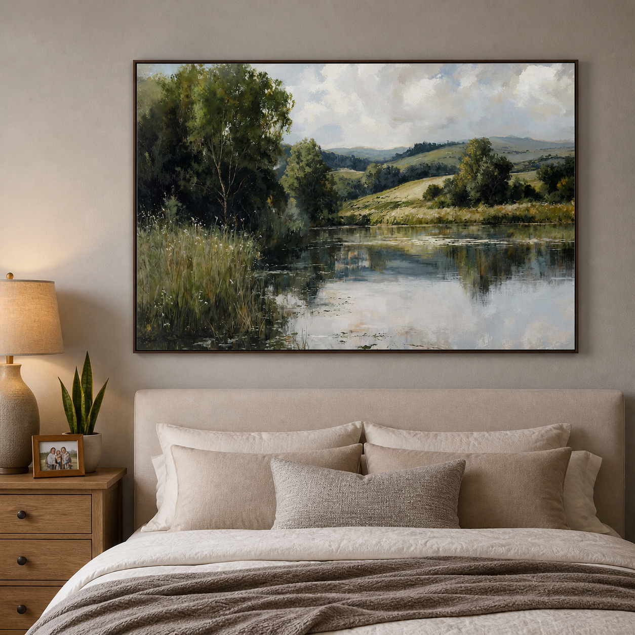 Leafy green trees and grasses beside a reflective lake with rolling hills and a cloudy blue sky, shown in a room setting