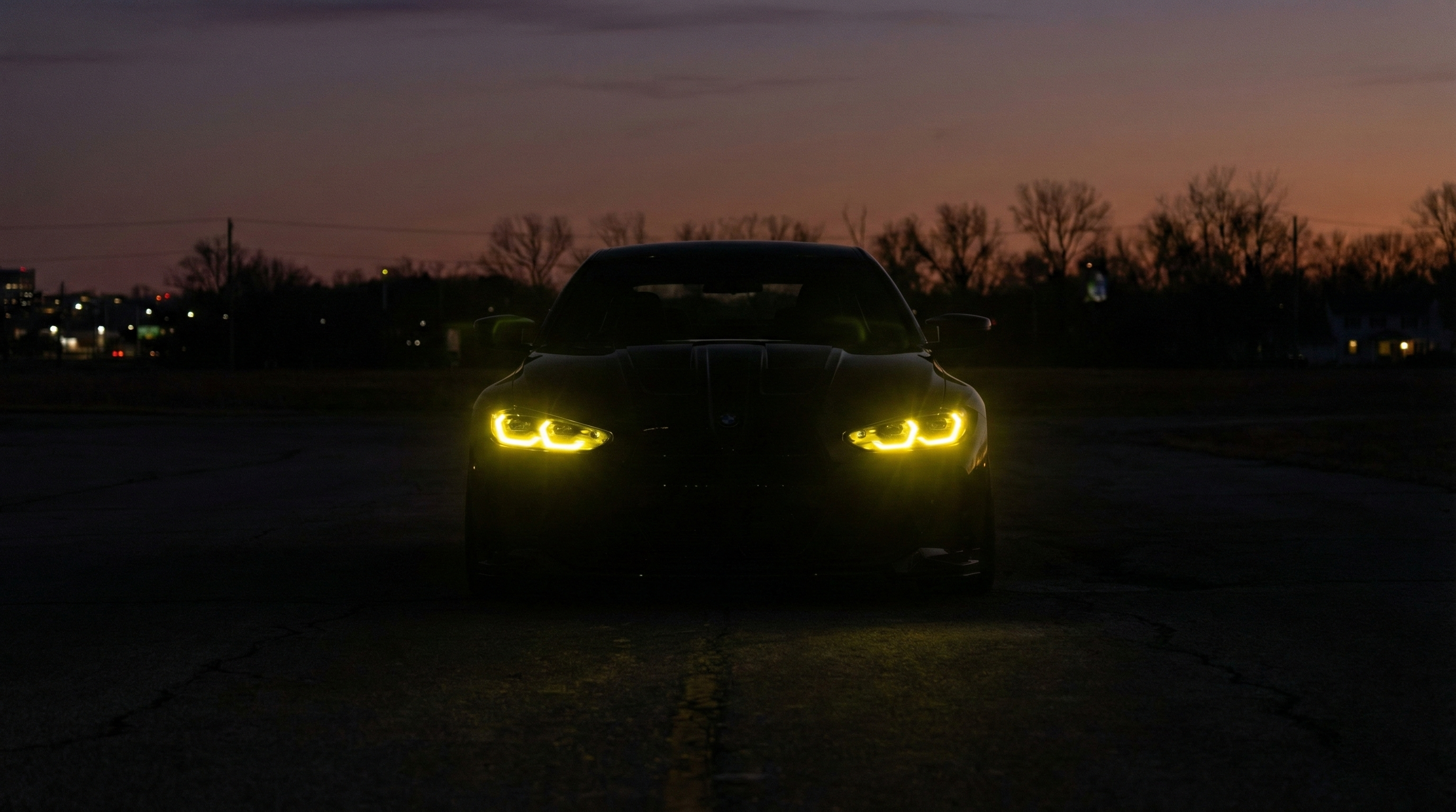 Front view of a BMW G82 M4 coupe at sunset with CSL-style yellow daytime running lights illuminated.