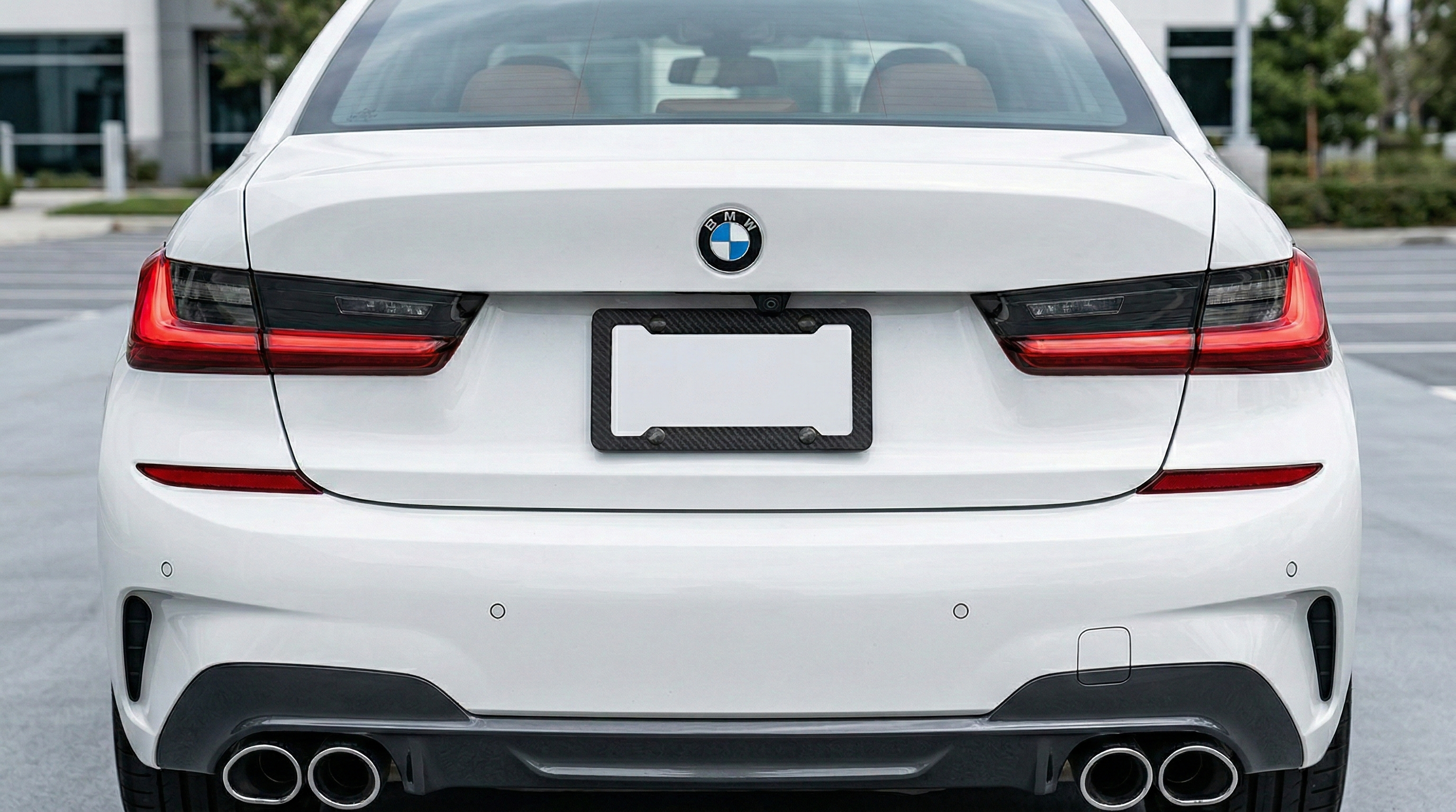 Real carbon fiber license plate frame installed on the rear bumper of a white BMW.