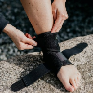 Woman adusting straps of ankle brace on a rock