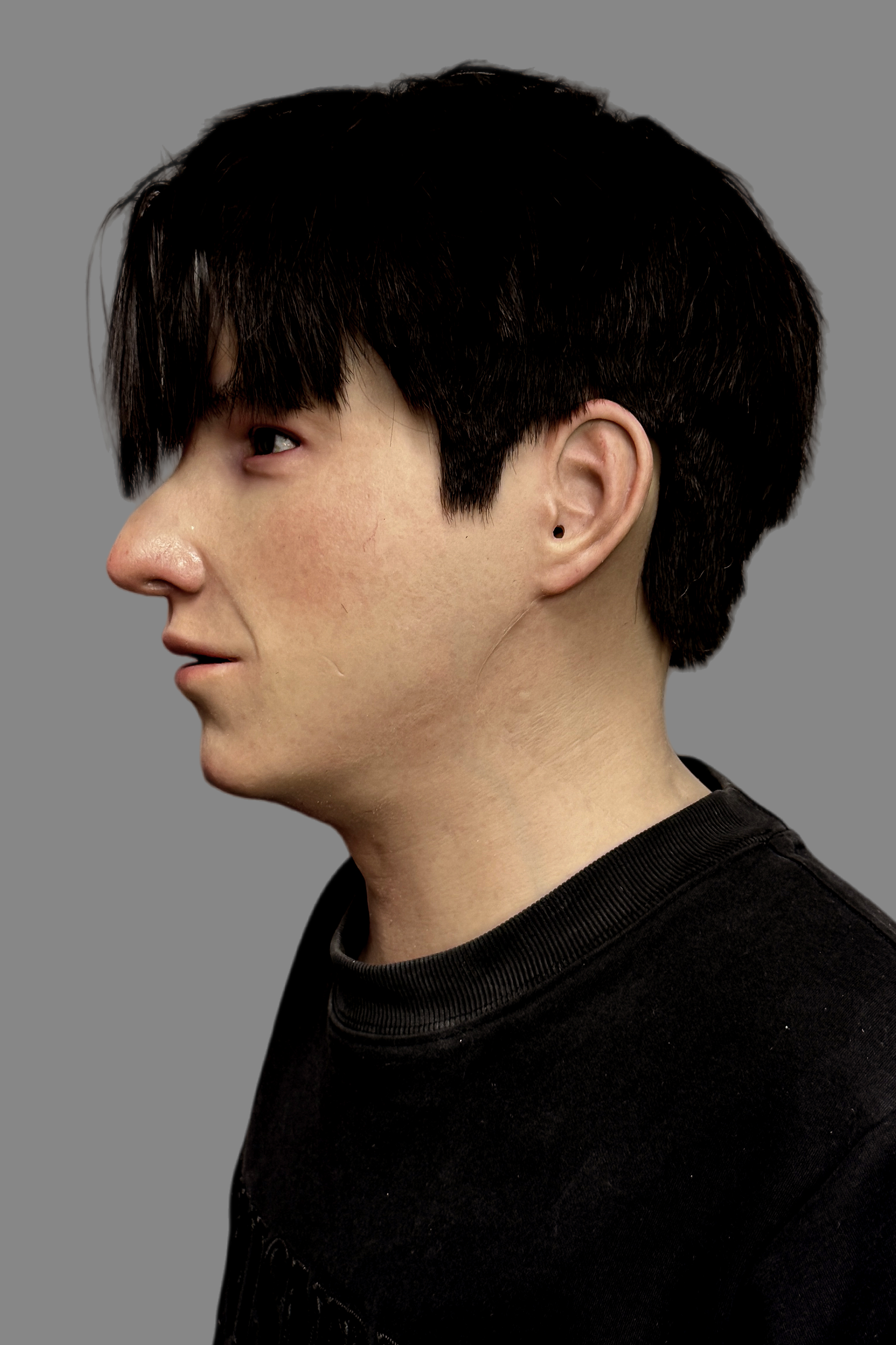 Three-quarter angle of lifelike young Asian man full-face silicone mask worn on model, showing seamless neck blend and real hair.