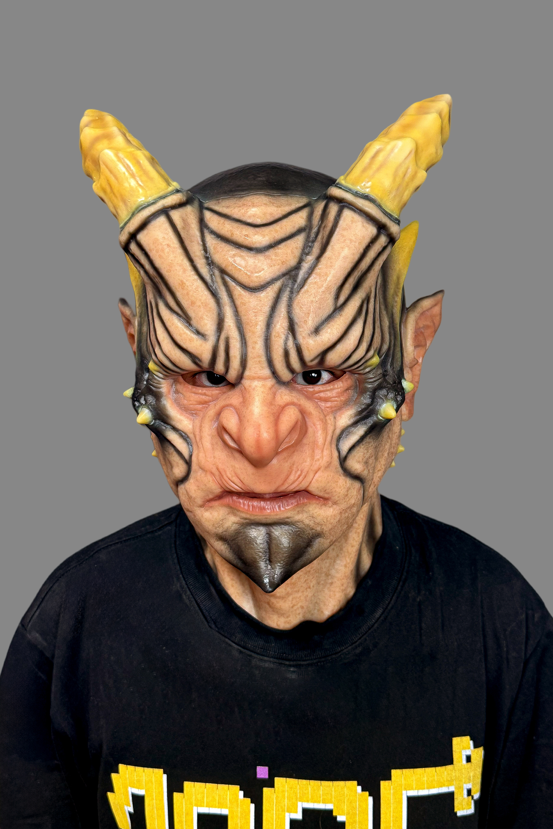 Ultra-lifelike horned demon silicone mask with yellow ram horns, black tribal tattoos, wrinkled skin and menacing scowl, worn on model
