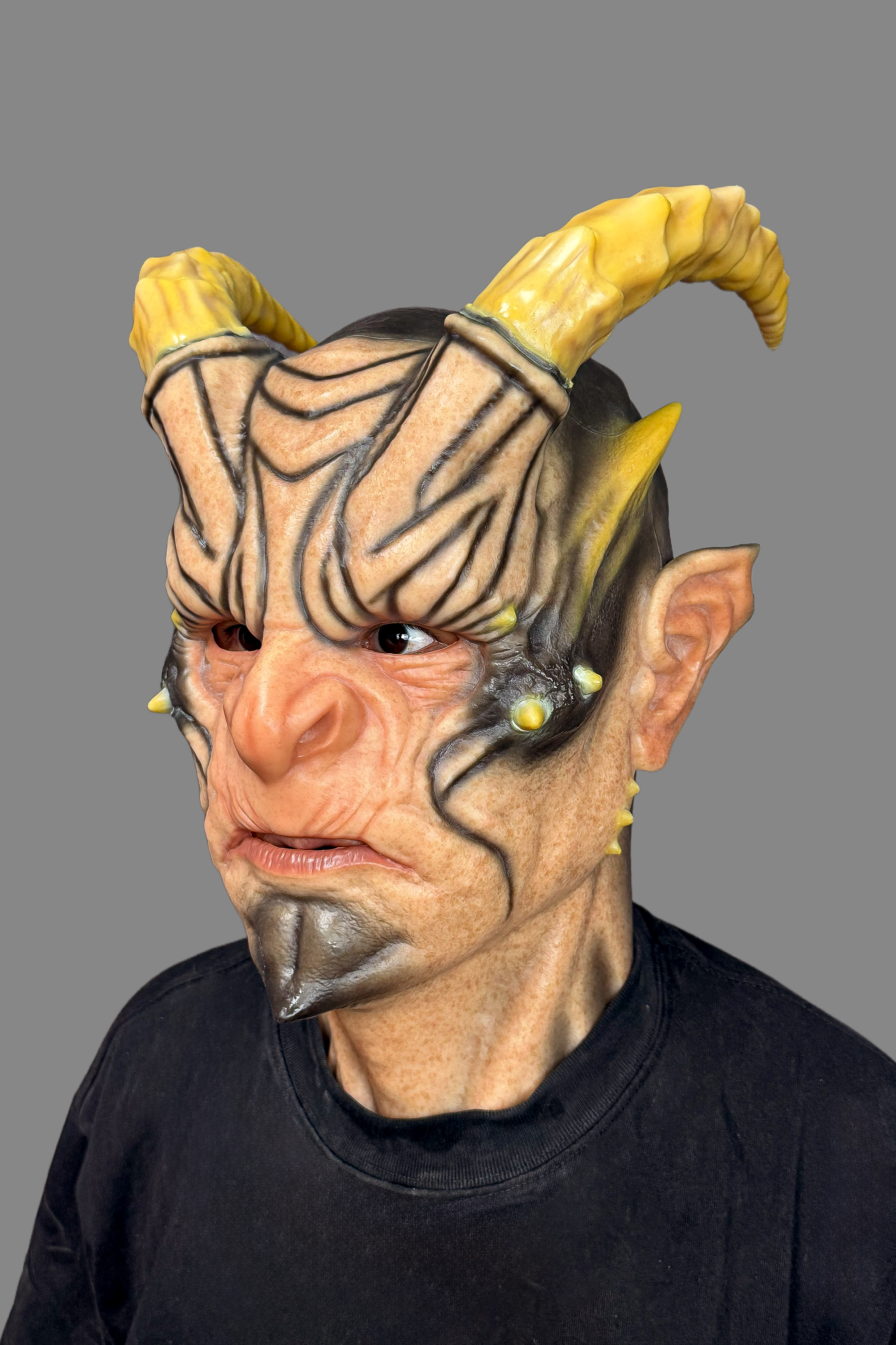 Professional horror demon latex mask featuring oversized yellow horns, black forehead stripes, goblin ears and open mouth design, front display.
