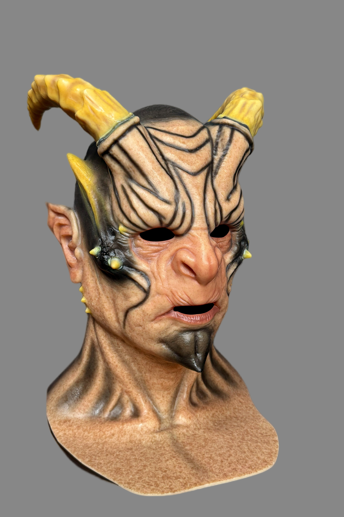 High-end demonic creature silicone mask with massive yellow horns, black tribal patterns, spiked facial protrusions and wrinkled neck, angled display.