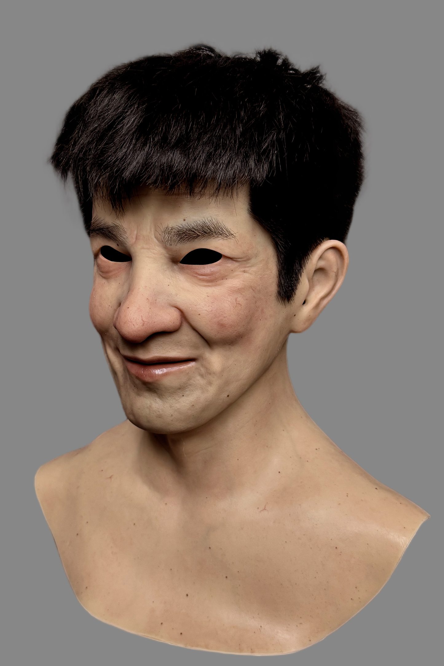 Premium hyper-realistic East male silicone disguise mask with hand-punched black hair and cheerful expression, front display.