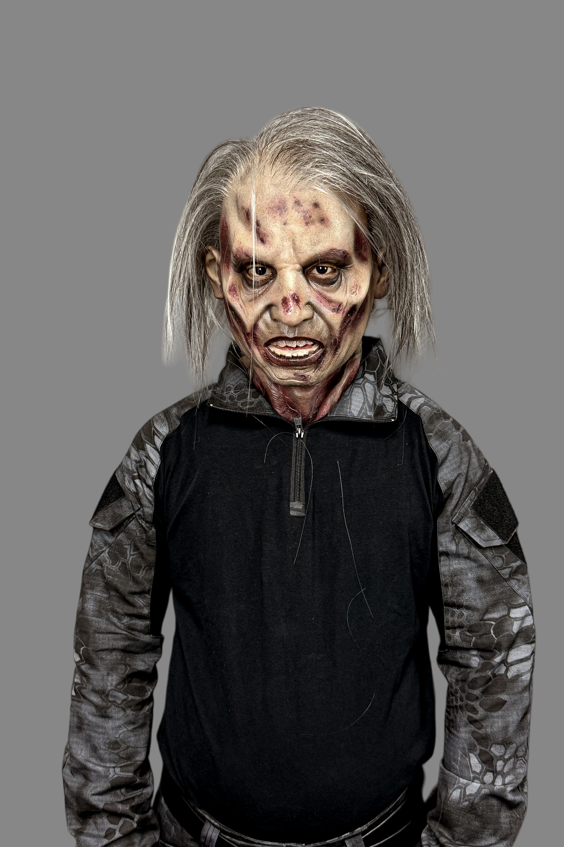 Ultra-detailed decaying zombie elderly male silicone mask featuring long white-gray hair and gory neck wounds, side view in tactical outfit.