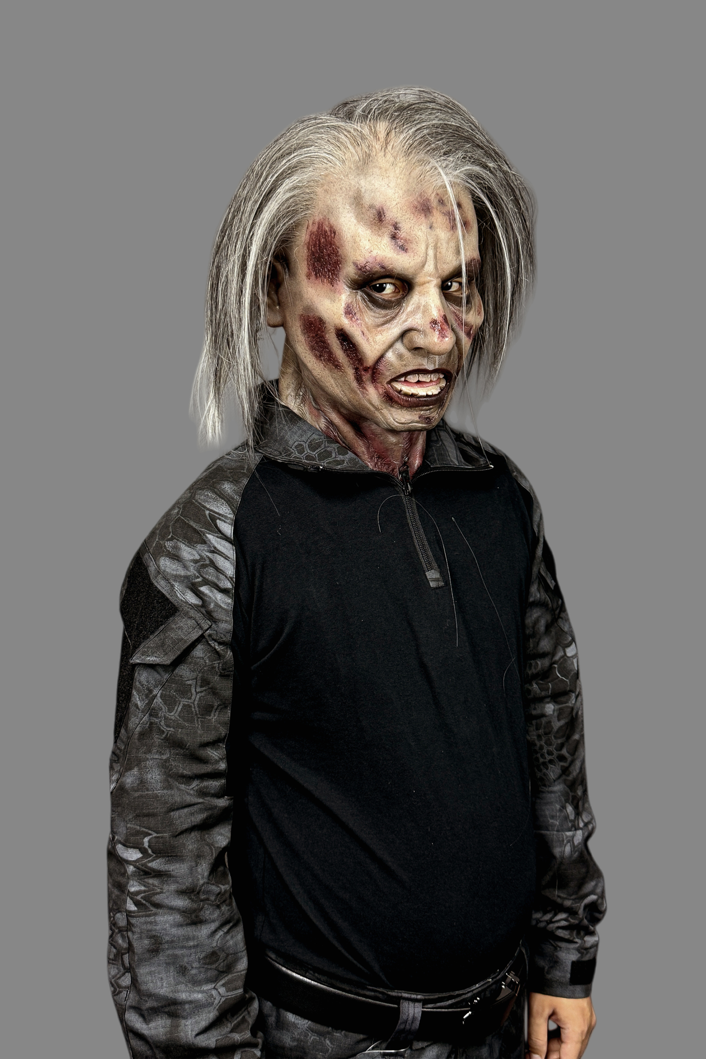 Terrifying zombie soldier silicone mask with rotting skin and long hair, paired with military plate carrier, tactical vest and combat gloves.