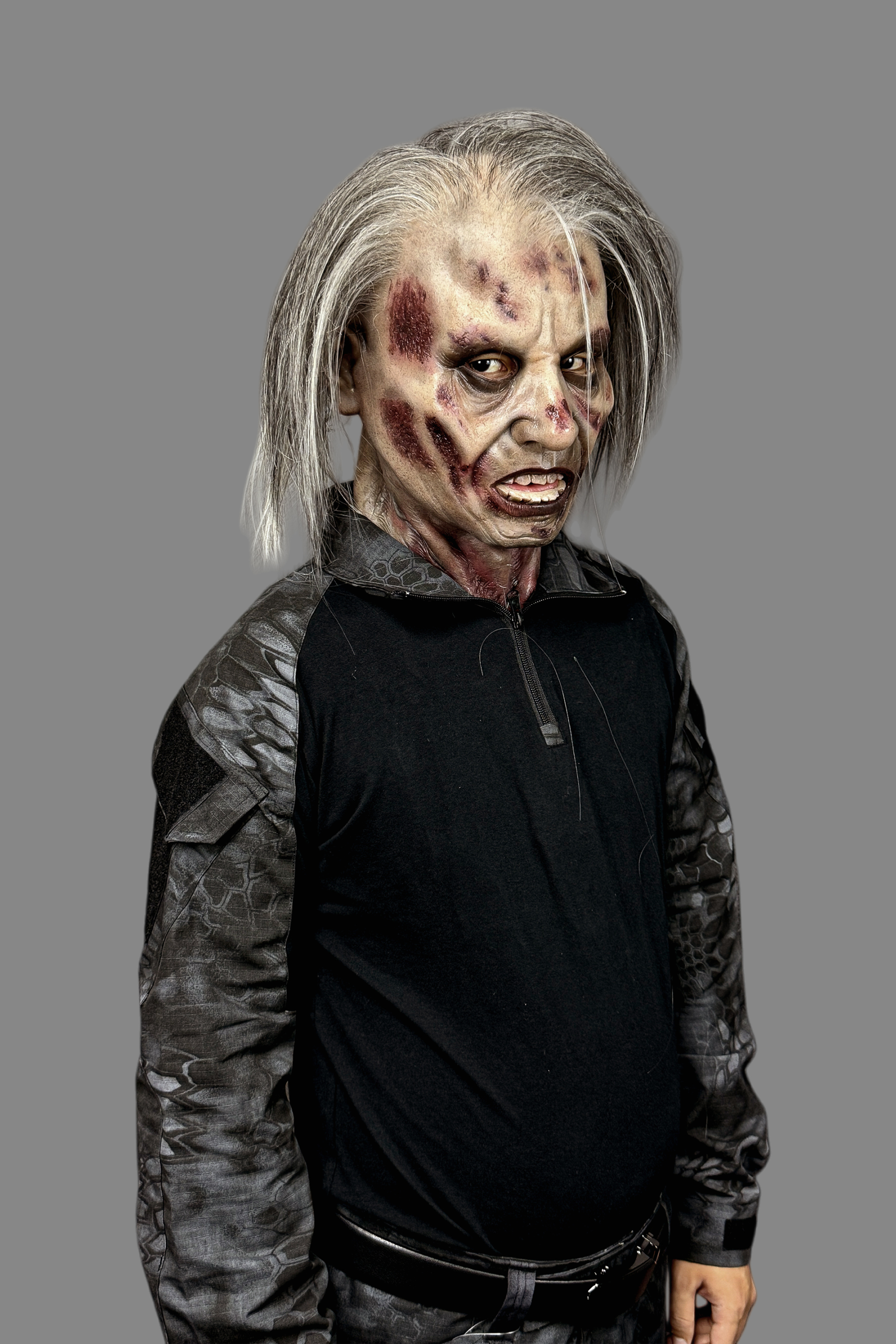 Terrifying zombie soldier silicone mask with rotting skin and long hair, paired with military plate carrier, tactical vest and combat gloves.