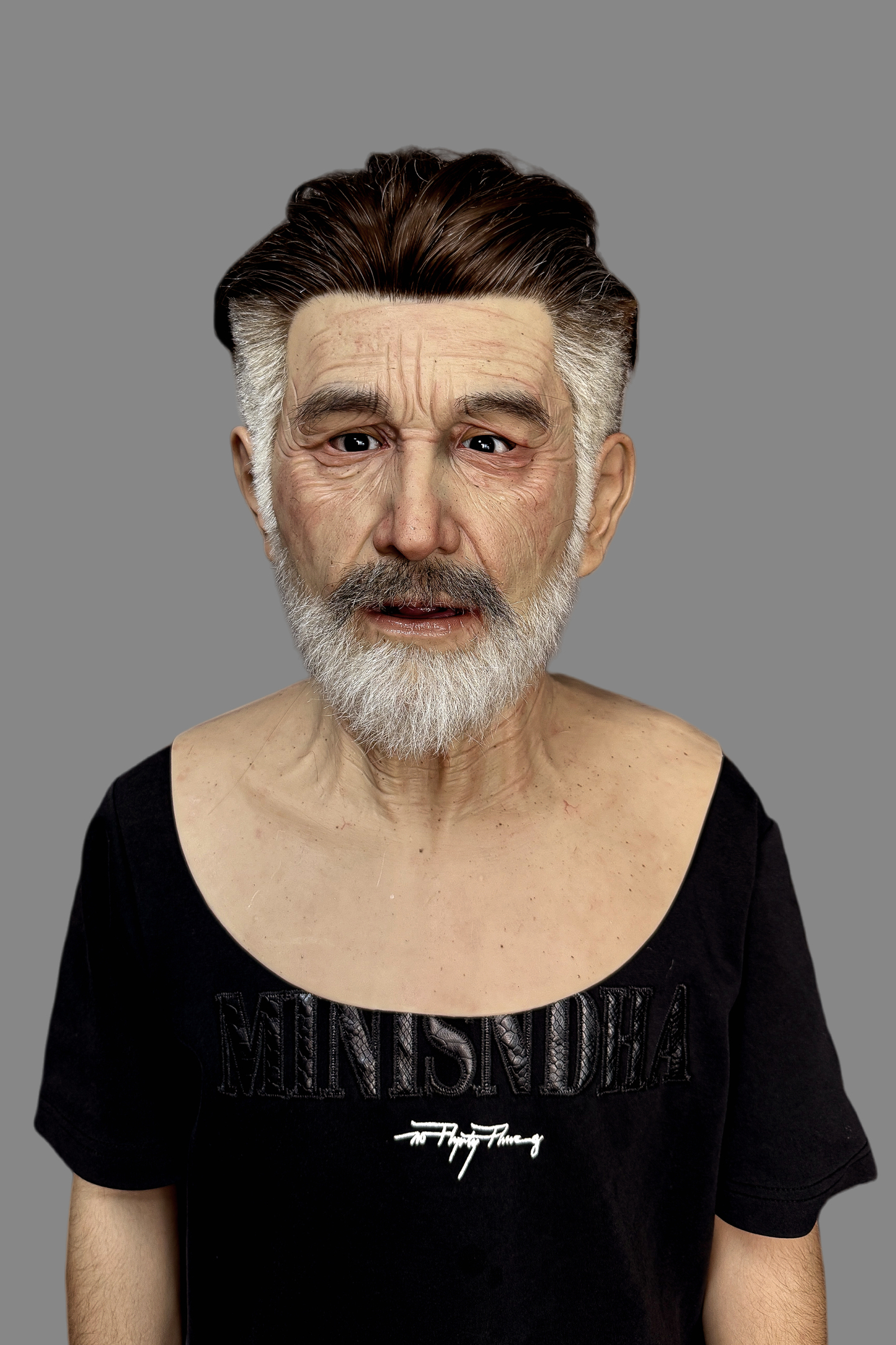 Hyper-realistic middle-aged Caucasian male silicone mask with slicked-back dark brown hair, gray temples, white beard and deep wrinkles, side view on model.