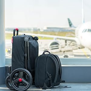 Imagen de carro plegado con estuche de viaje en una terminal de aeropuerto. Pequeña mochila negra está al lado del vagón