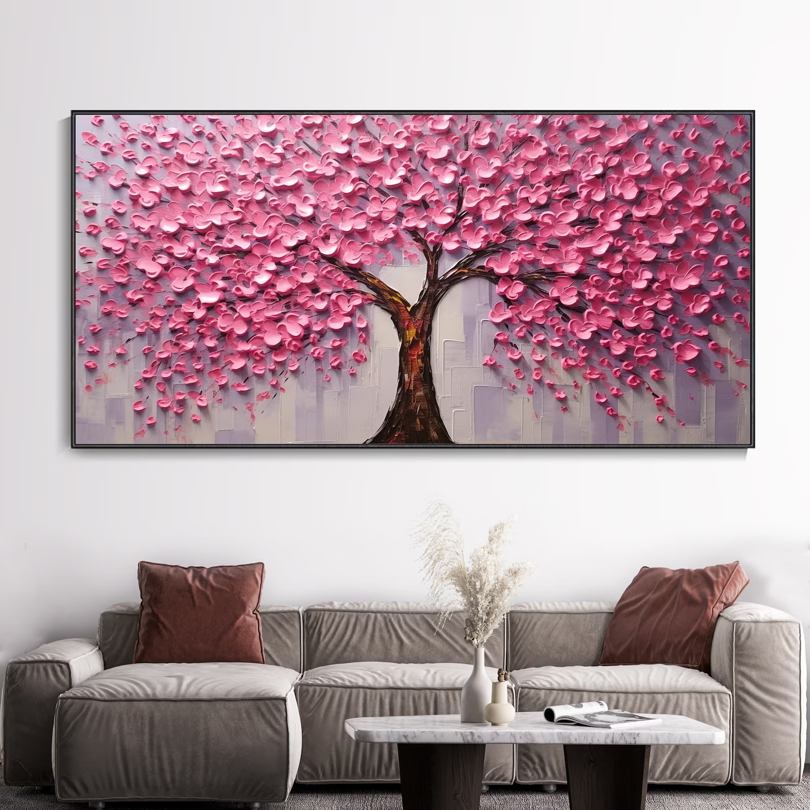 Modern pink floral tree abstract painting hanging above a grey sofa in a contemporary living room, with a white marble coffee table and dried flower vase.
