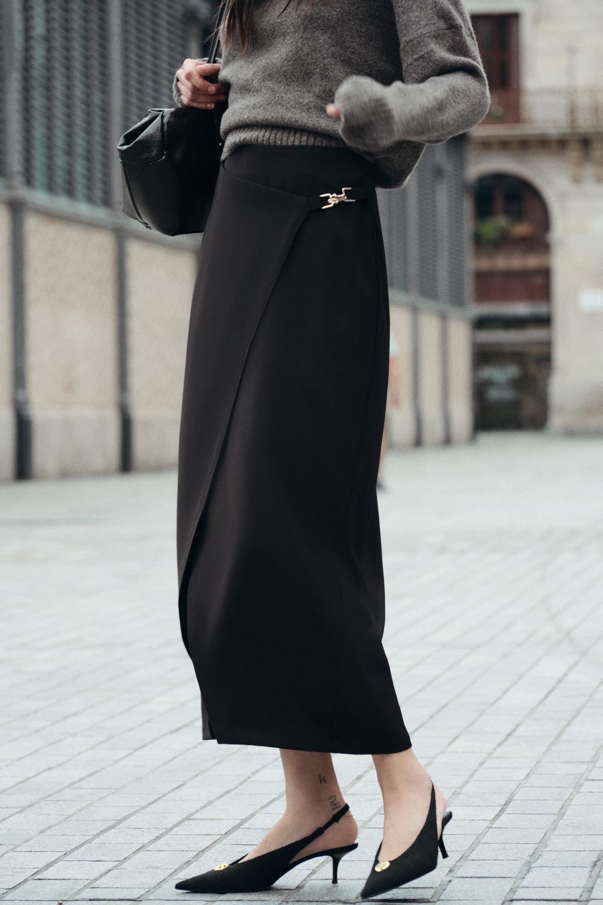 High waisted skirt with front slit. Wrap closure with hidden interior button and golden clip appliqu.