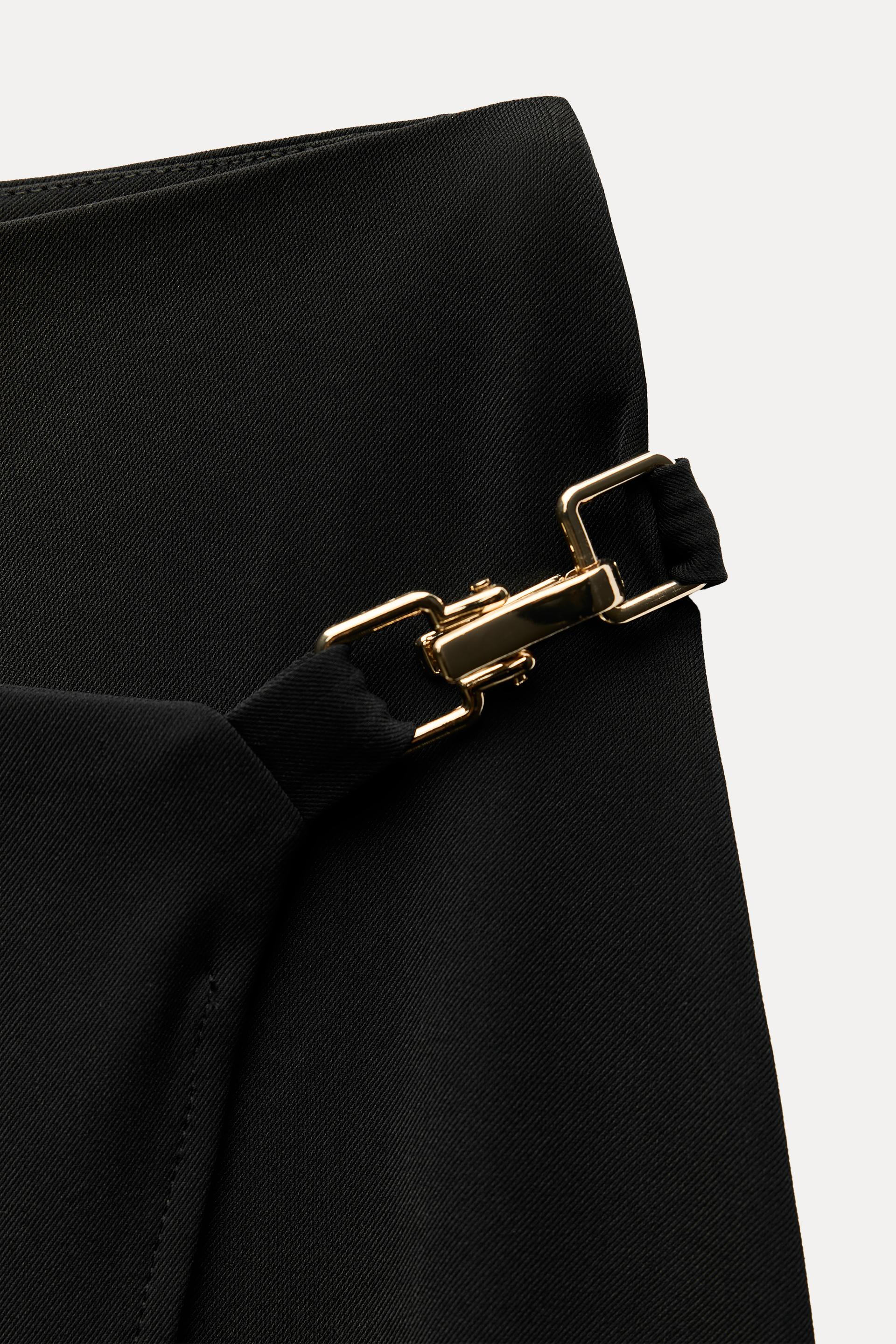 High waisted skirt with front slit. Wrap closure with hidden interior button and golden clip appliqu.