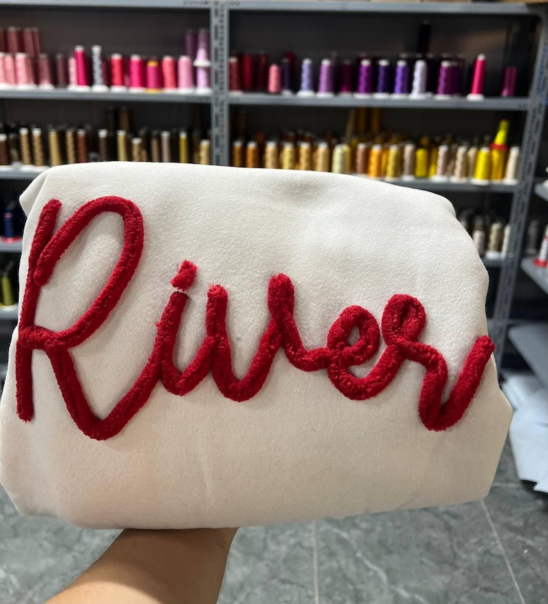 May include: A white sweatshirt with the word 'River' embroidered in red thread.