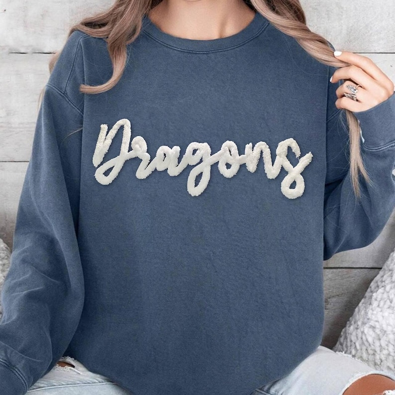 May include: A blue sweatshirt with a white, fluffy, cursive word 'Dragons' on the front.