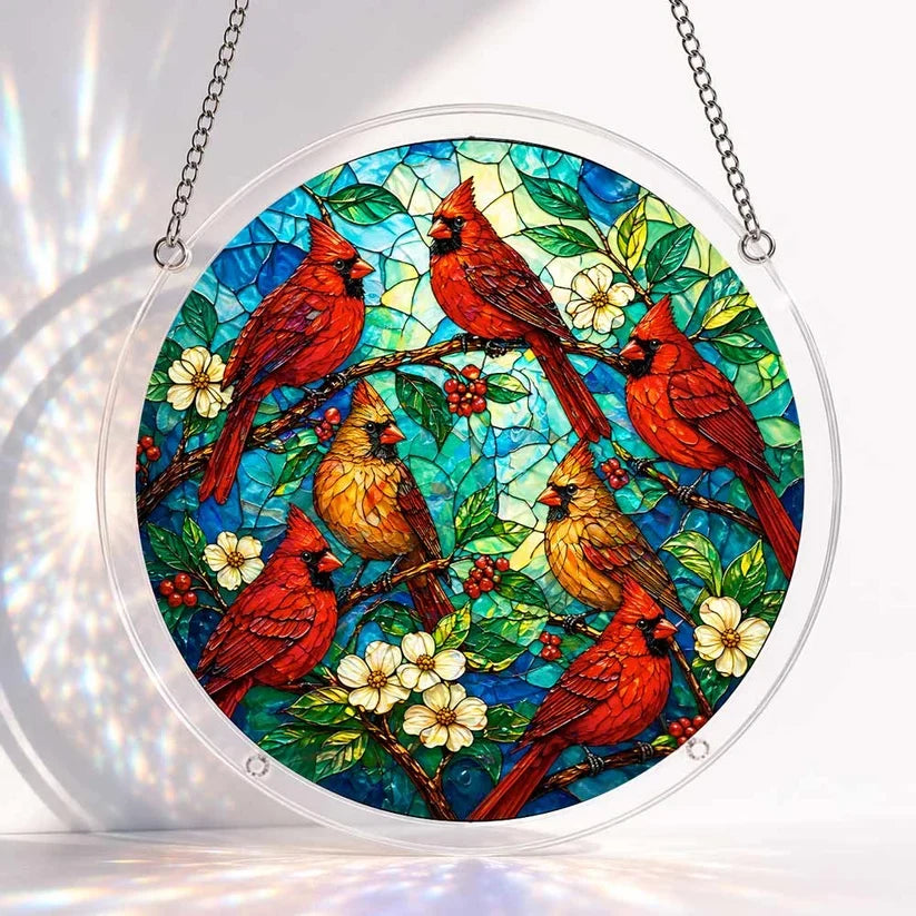 A round acrylic suncatcher with red and yellow cardinal birds perched among white blossoms berries and green leaves