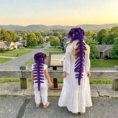 A woman and a child wearing matching purple dinosaur skeleton costumes, viewed from behind as they stand outdoors at a scenic overlook with a town and mountains in the distance.