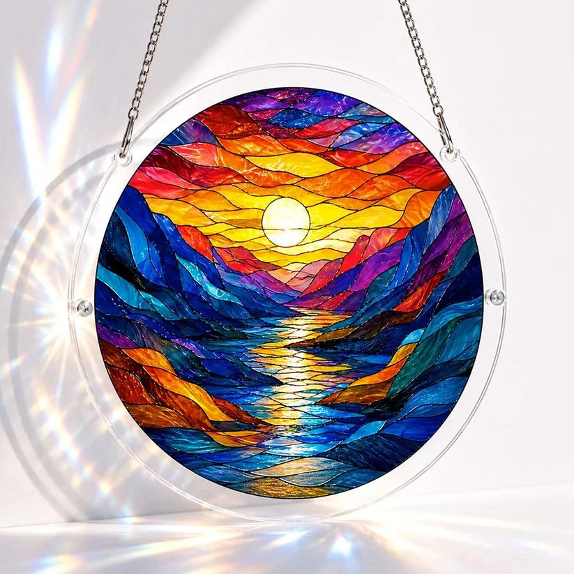 A round acrylic suncatcher of a colorful stained glass mountain river valley at sunset with the sun reflected on water