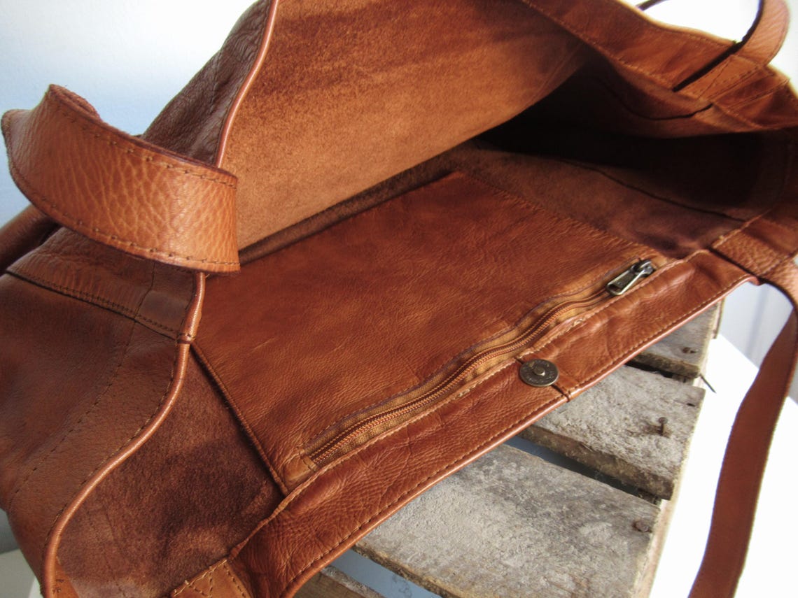 May include: A brown leather tote bag with a zippered closure and an inside pocket. The bag is made of high-quality leather and has a spacious interior. It features a sturdy shoulder strap and a classic design, suitable for everyday use.