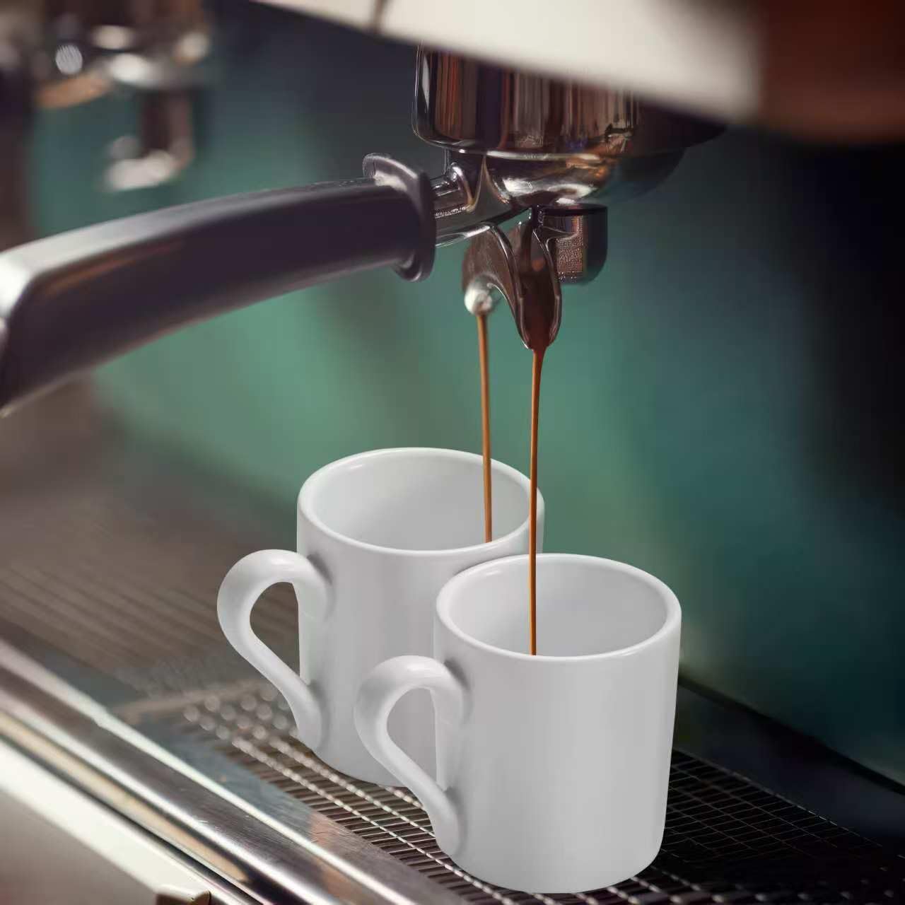 Set of two white ceramic espresso cups placed under an espresso machine