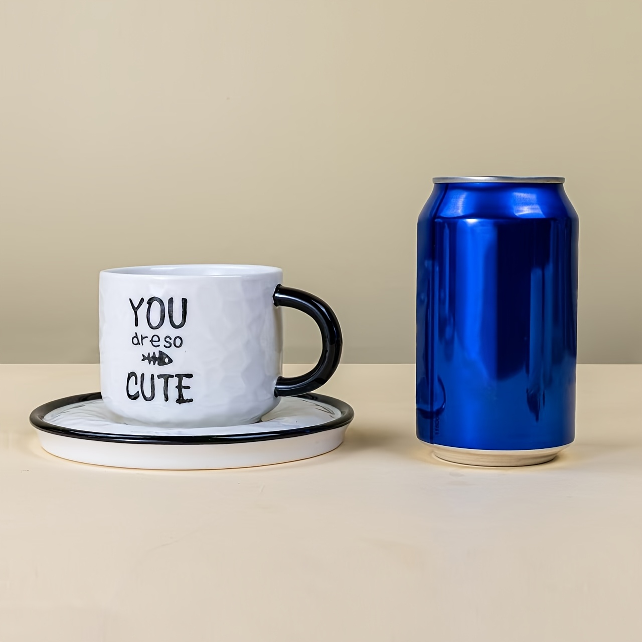 Ceramic cat mug with saucer beside blue can for size reference