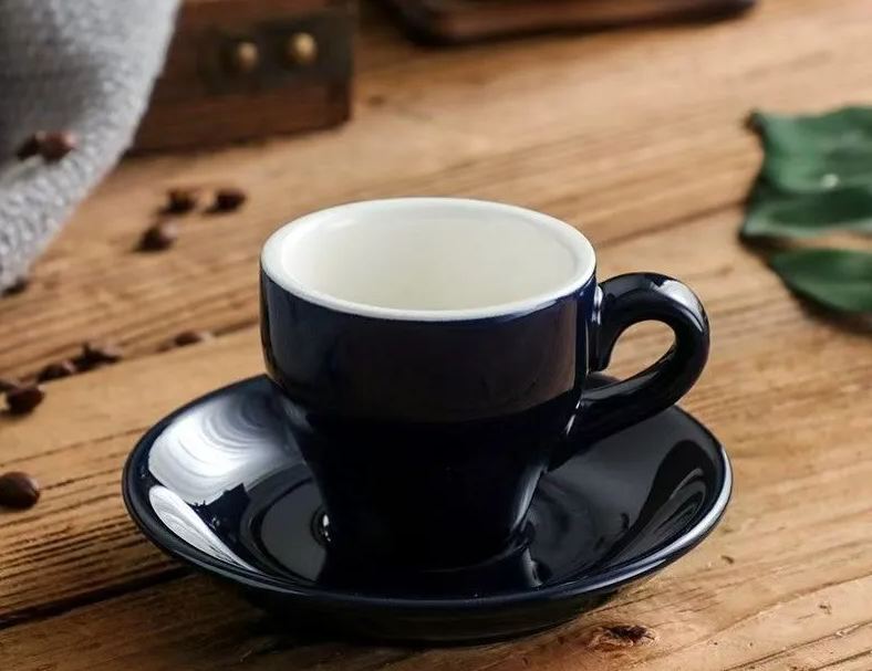 Black ceramic 2.5 oz espresso cup with matching saucer on a wood table