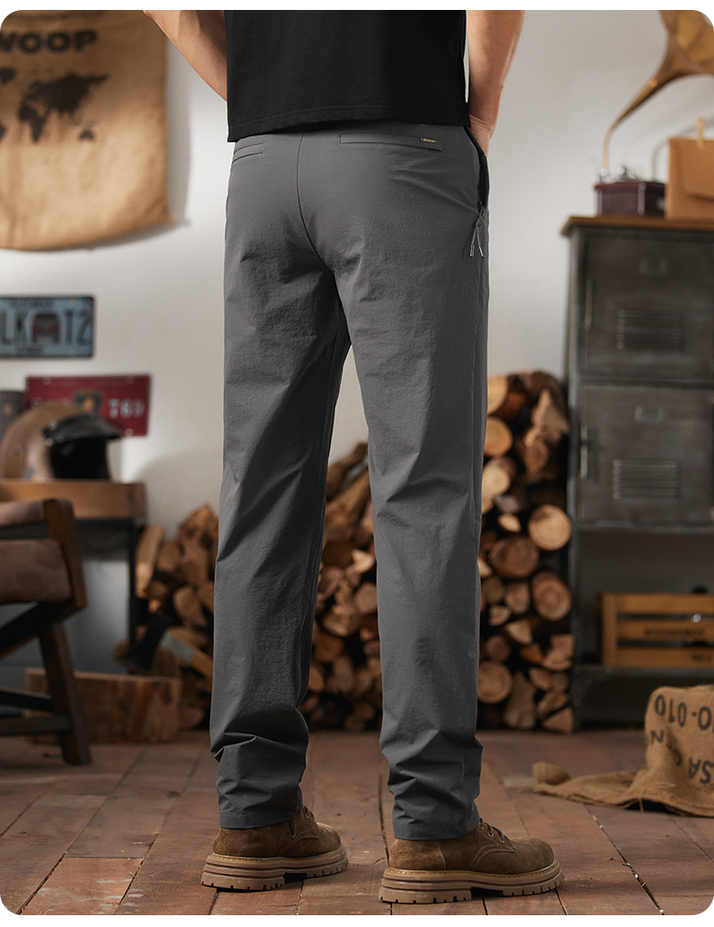 Rear view of AFTCO Honcho tactical utility pants in dark gray, paired with tactical boots in a rustic workshop setting.