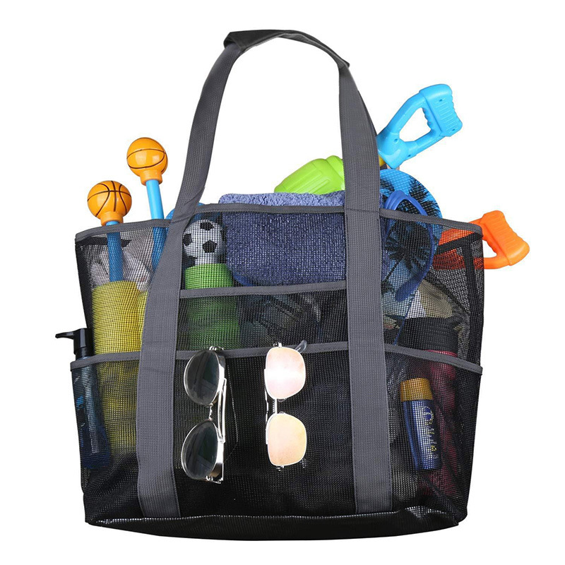 Front view of a large black mesh beach tote bag with exterior pockets holding sunglasses, beach toys, and towels.