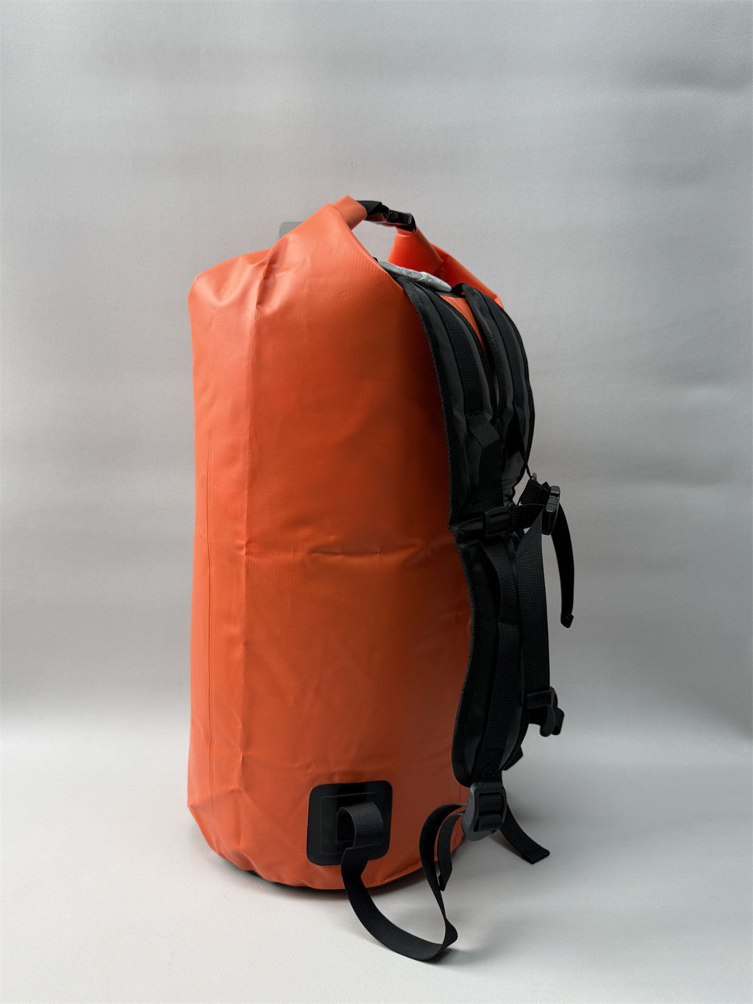 Side angle of the orange 40L marine dry backpack showing the rolled top buckle closure and reinforced base.