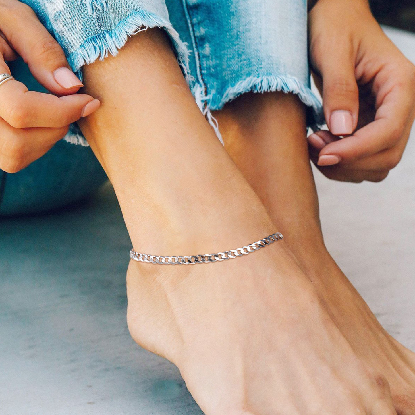 Simple silver chain anklet worn on ankle with frayed blue jeans