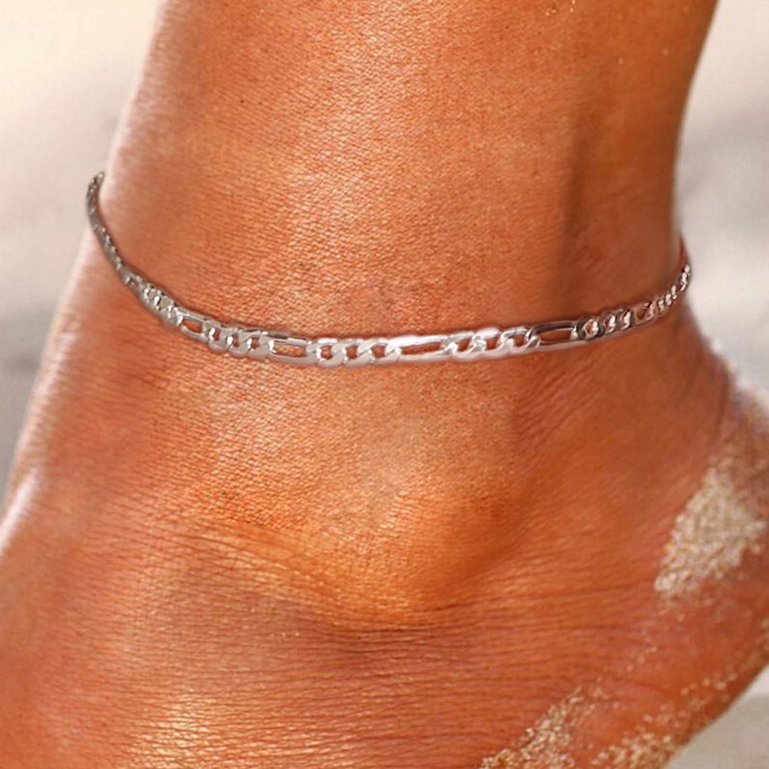 Close-up of a silver chain anklet on ankle with sand grains