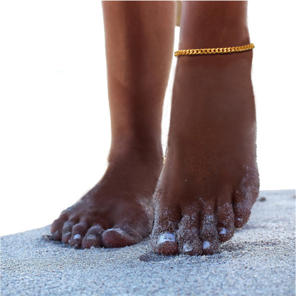 Close-up of foot with gold chain anklet on sandy beach