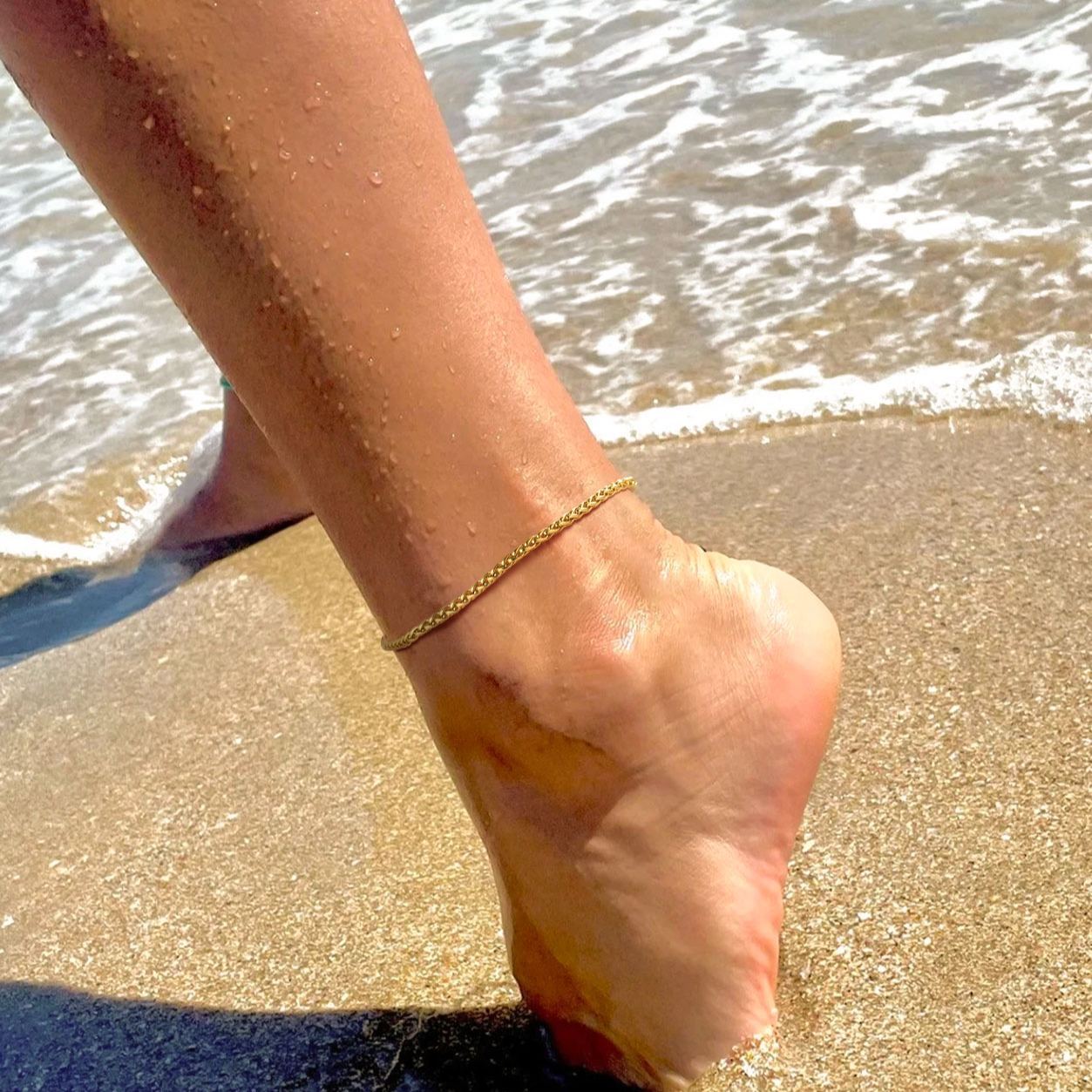 Gold ankle chain on wet sandy foot