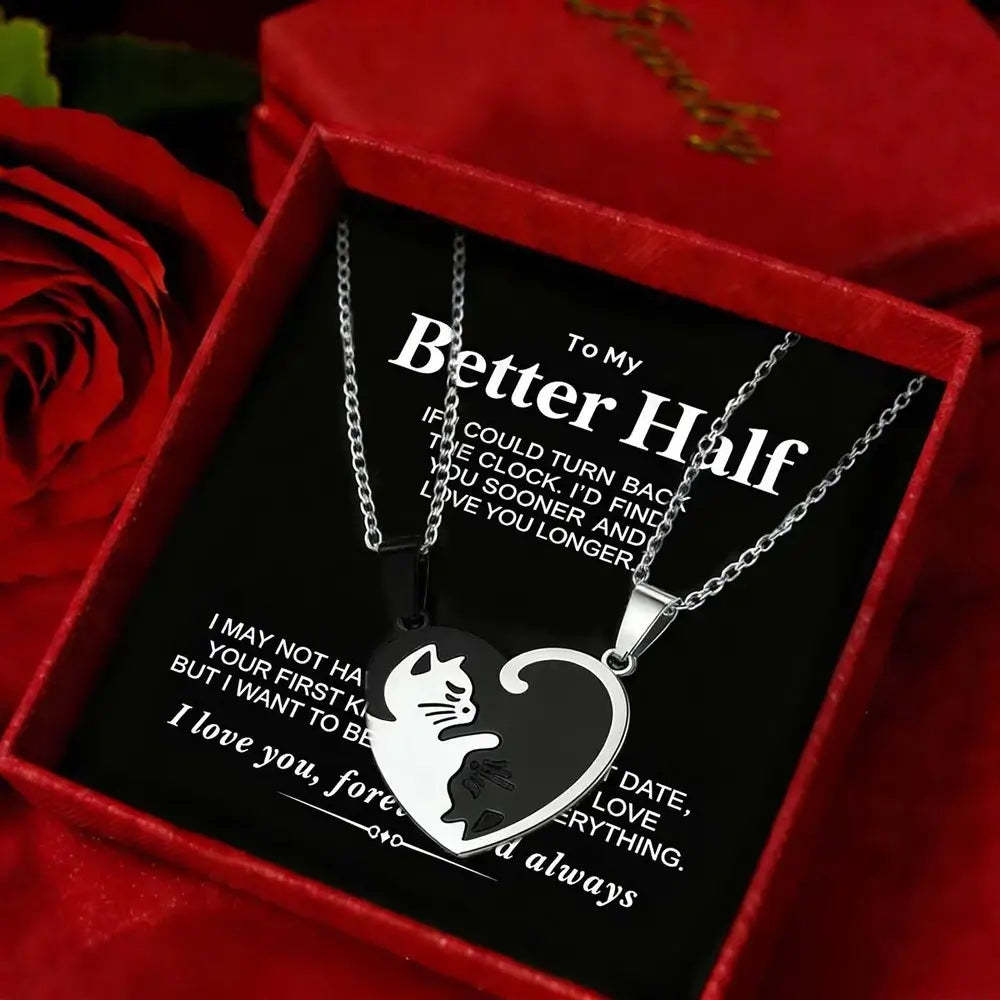 A silver heart-shaped pendant necklace with a cat silhouette cutout, displayed inside a red gift box with a black message card. Red roses are visible in the background.