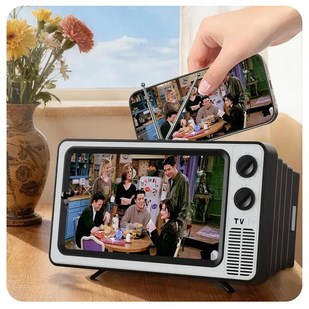 Small TV-like device displaying a scene from a show, held by a hand above a table with flowers.