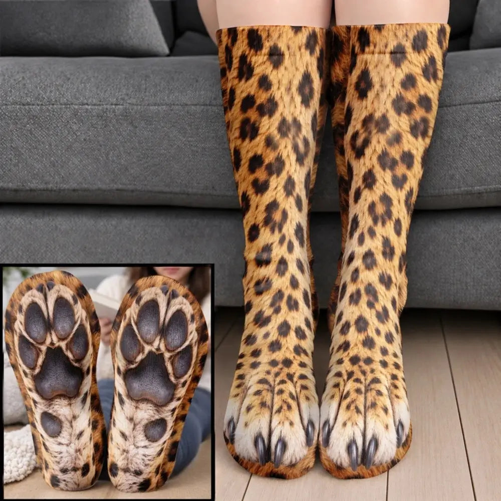 Yellow leopard spotted paw socks with dark paw pads worn on legs before a gray sofa
