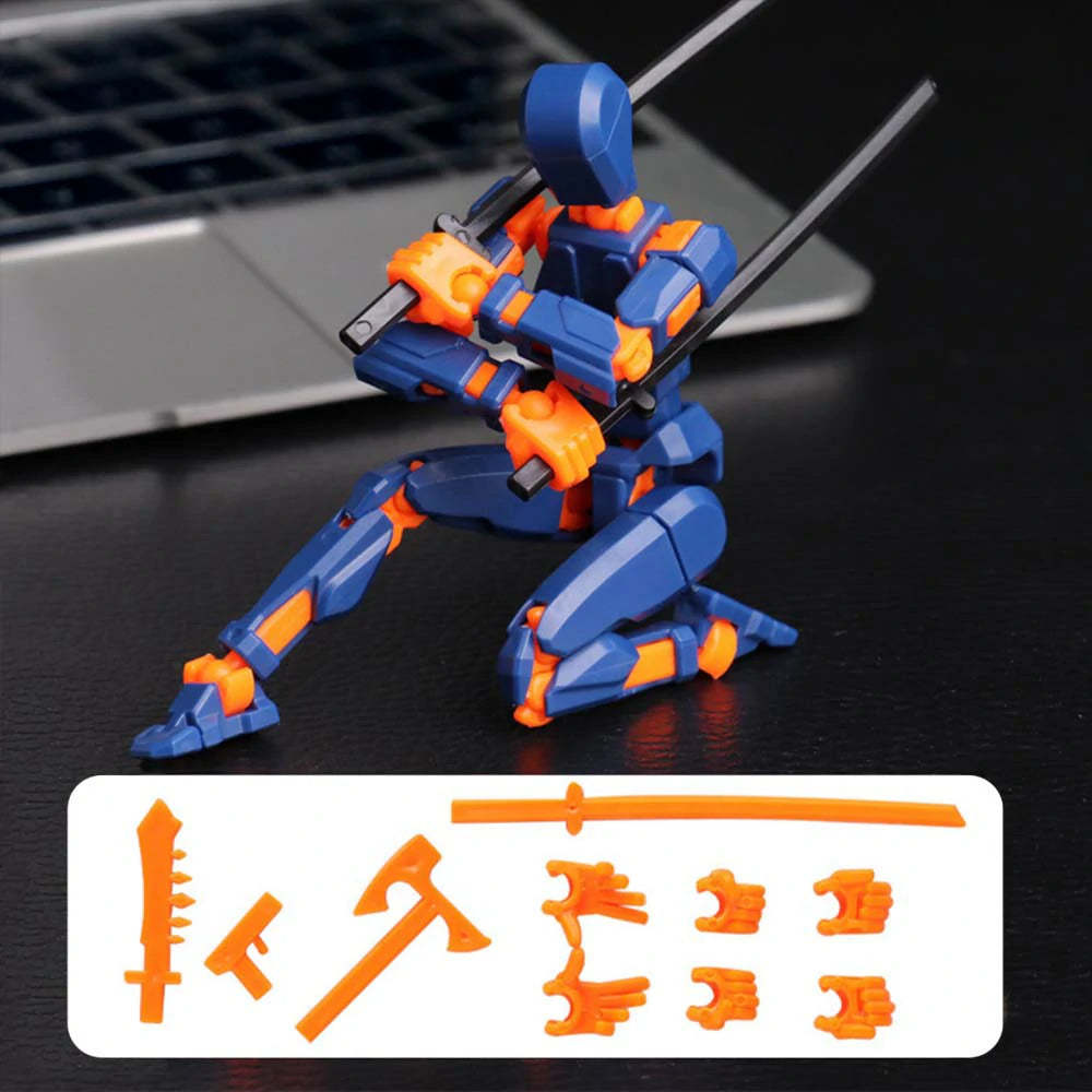 A blue and orange plastic robot action figure posed kneeling on a dark tabletop with a laptop blurred in the background. A white label at the bottom shows additional orange accessory pieces.