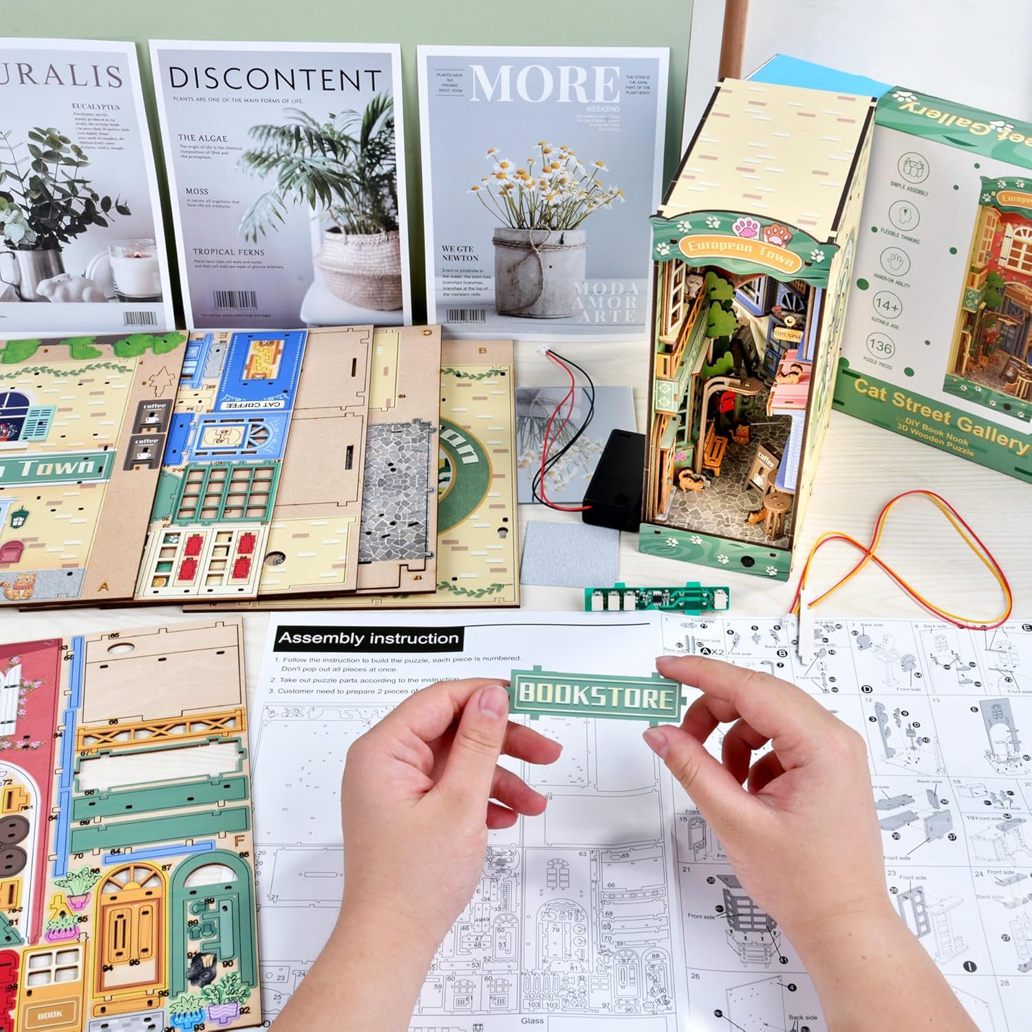Hands holding the 'Bookstore' sign part for the DIY book nook, with wooden sheets and mirror sheet in background.-uFunSpace