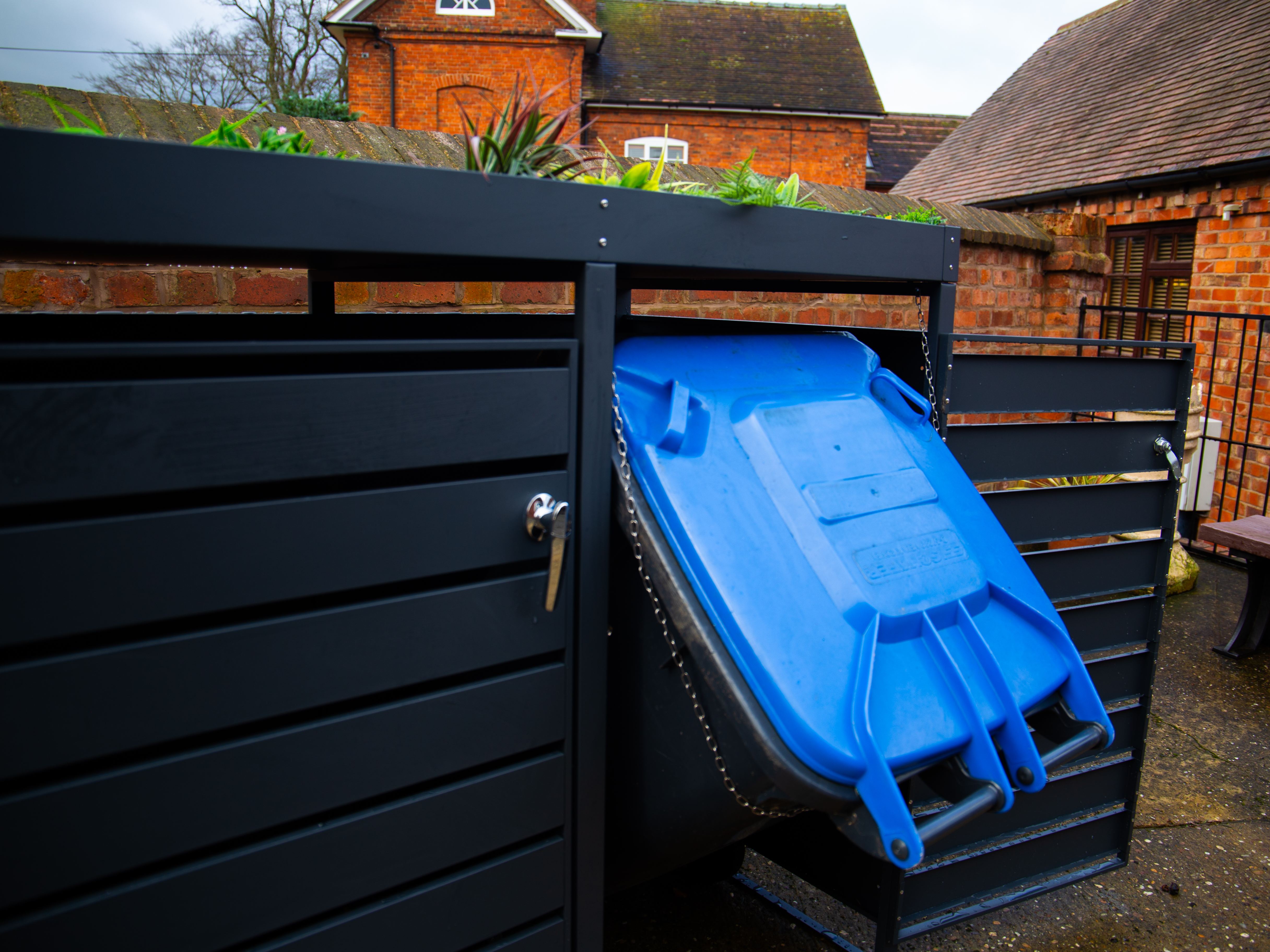 Anthracite bin store with blue wheelie bin partially pulled forward, chain lid support visible
