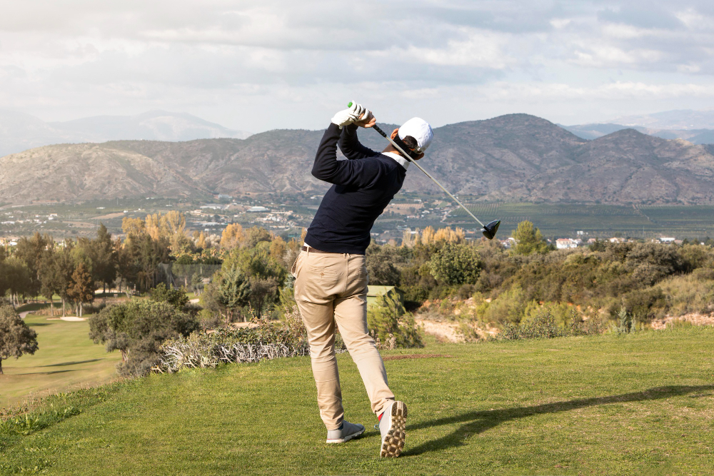 Gloved golfer mid-swing on a course with mountains and trees in the background