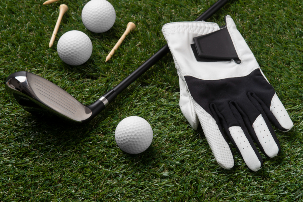 Golf glove, balls, tees, and a driver laid out on green grass