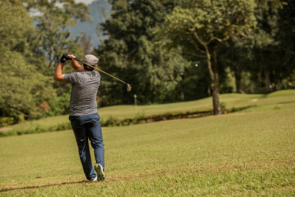 Golfer mid-swing on a sunny course with trees in the background